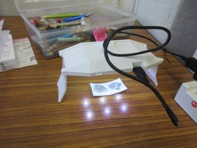 子どもたちのイラストに3Dジェルを乗せてLEDライトで硬化している様子の写真