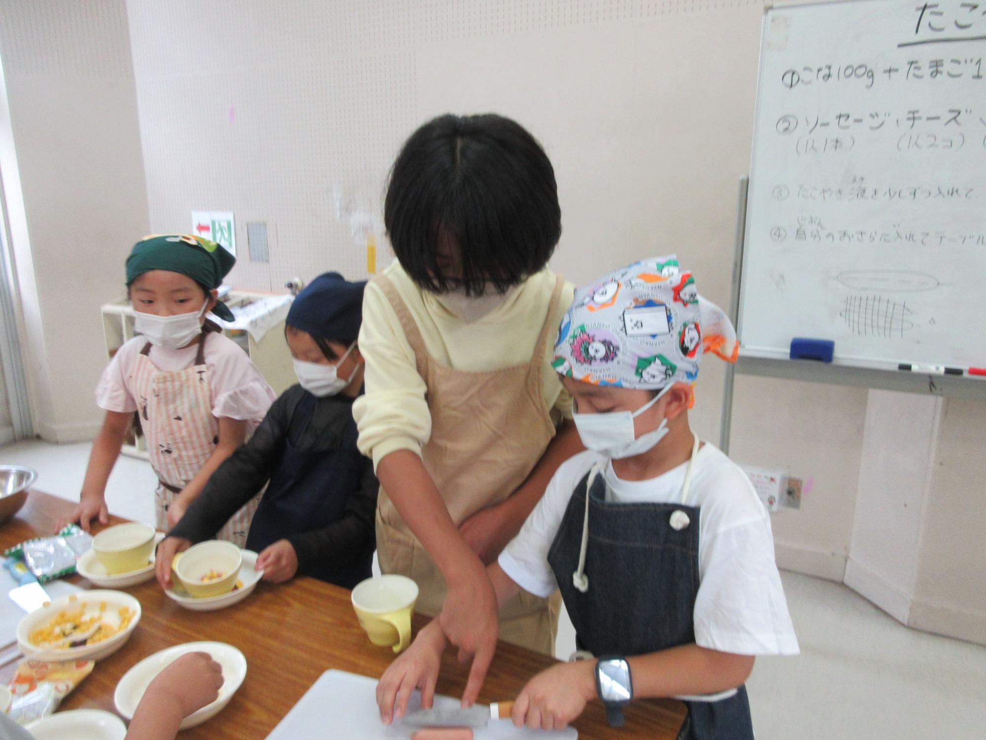 中学生がお手伝いで小学生に切り方を教えている様子の写真