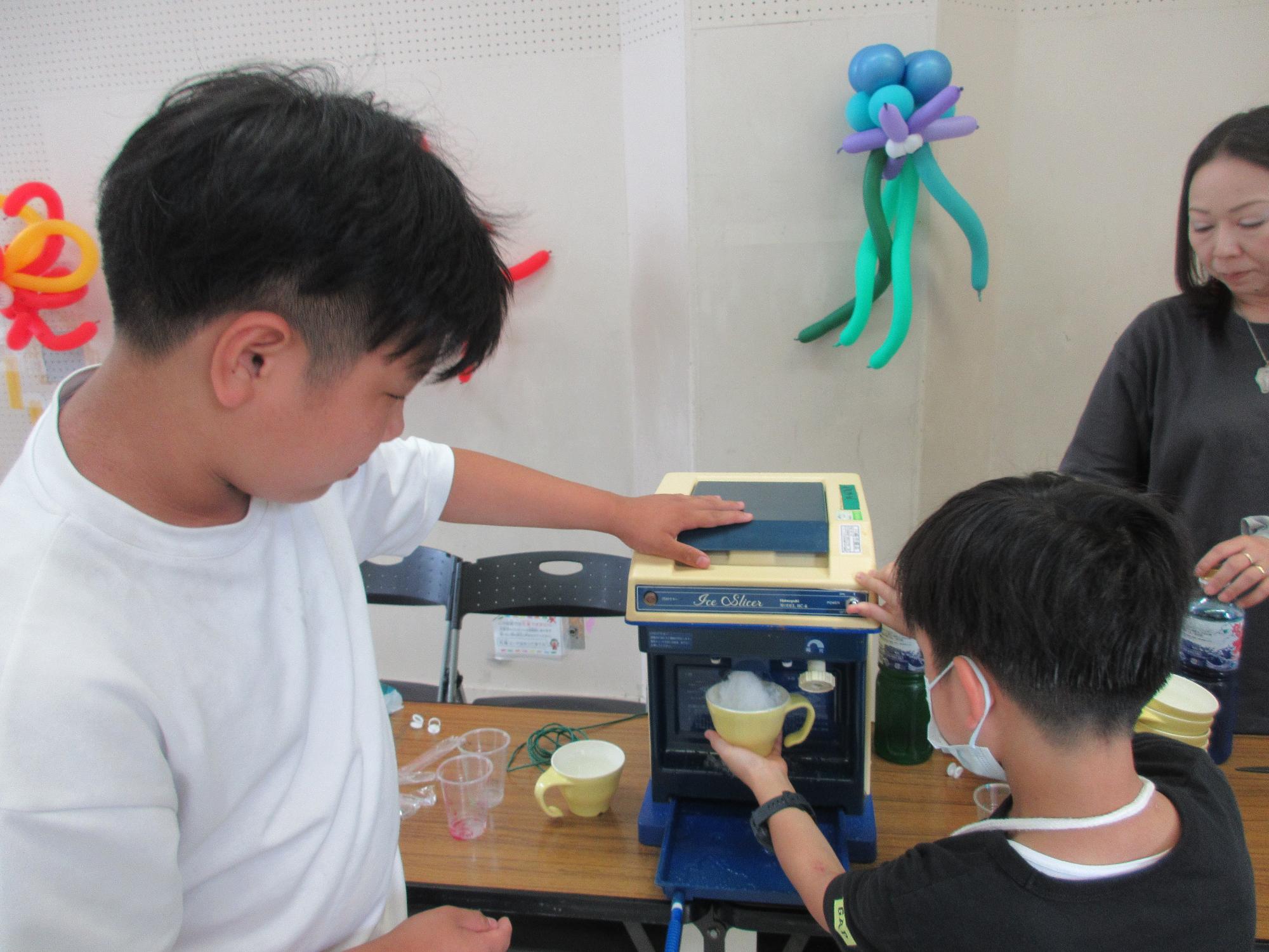 中学生に見守られながら自分でかき氷機を動かしている小学生の様子の写真