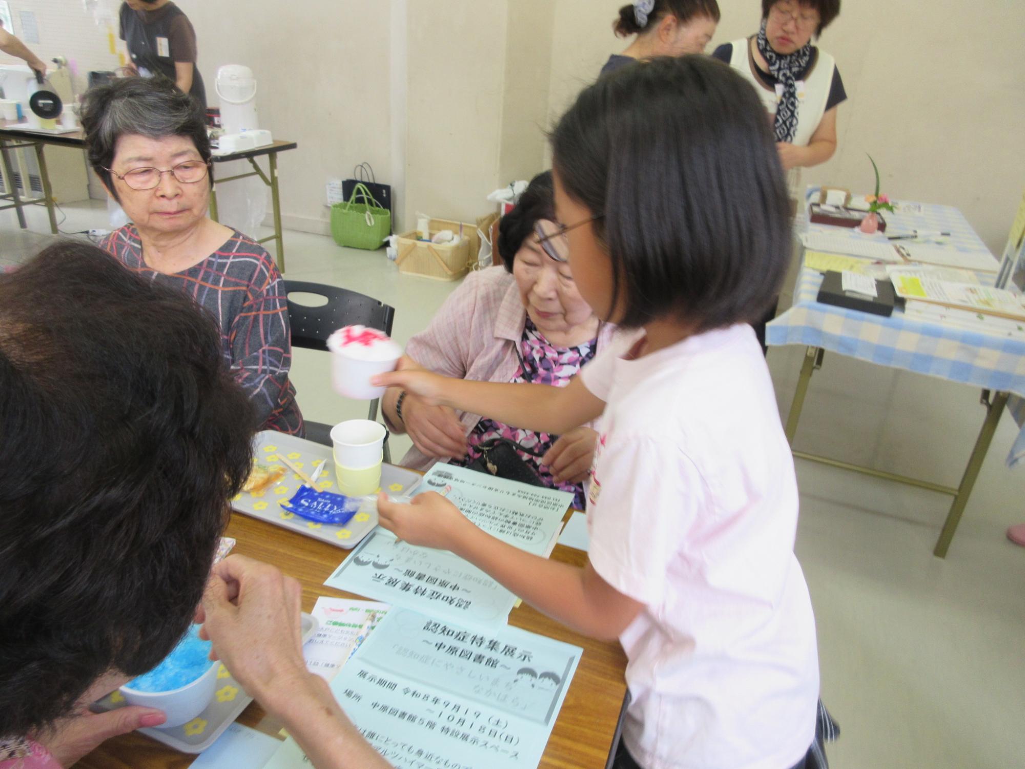 出来上がったかき氷を参加した地域の方に運んでいる小学生の様子の写真