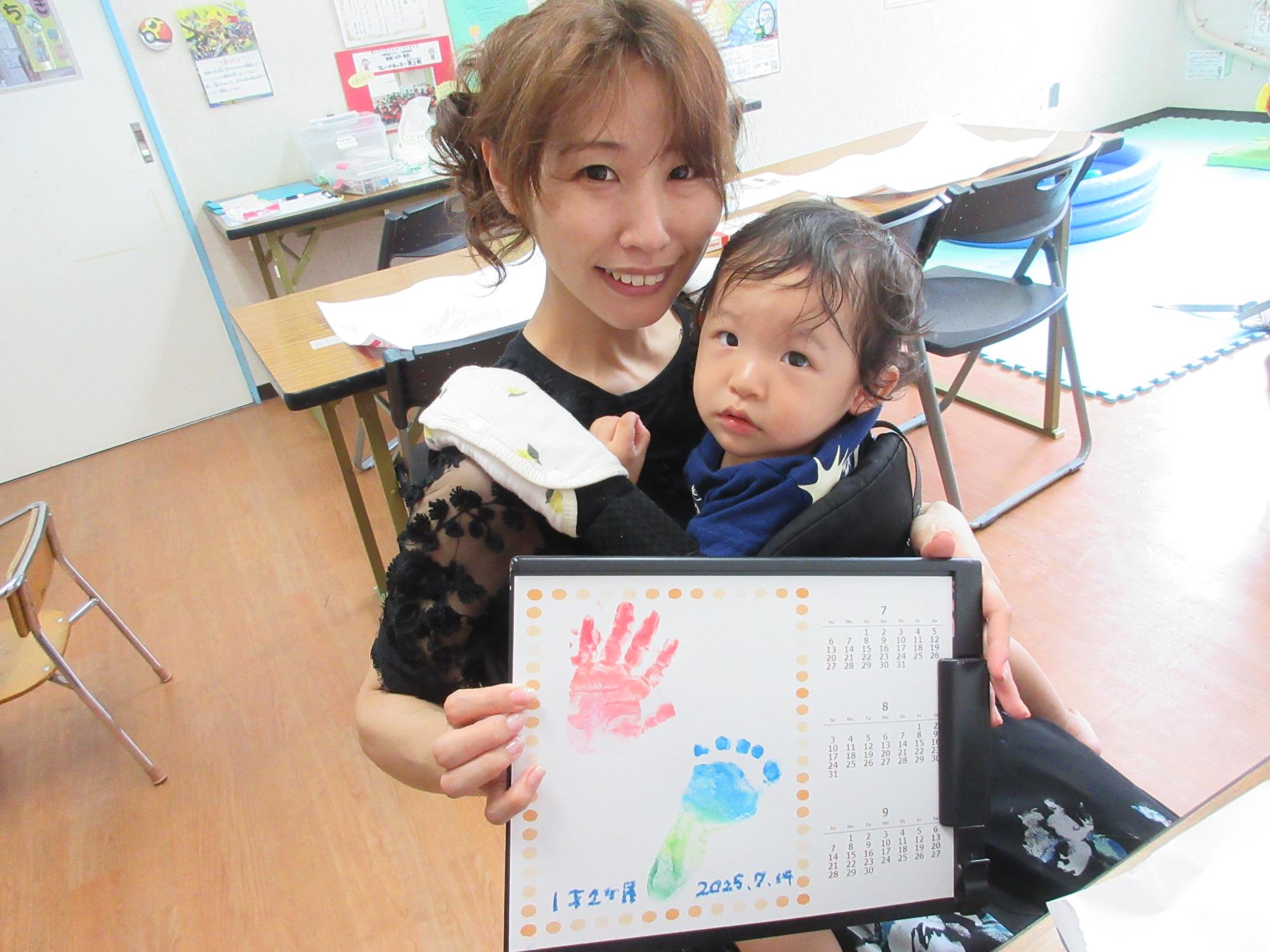 綺麗なグラデーションの手形、足形で作ったカレンダーを持っている幼児親子の様子の写真