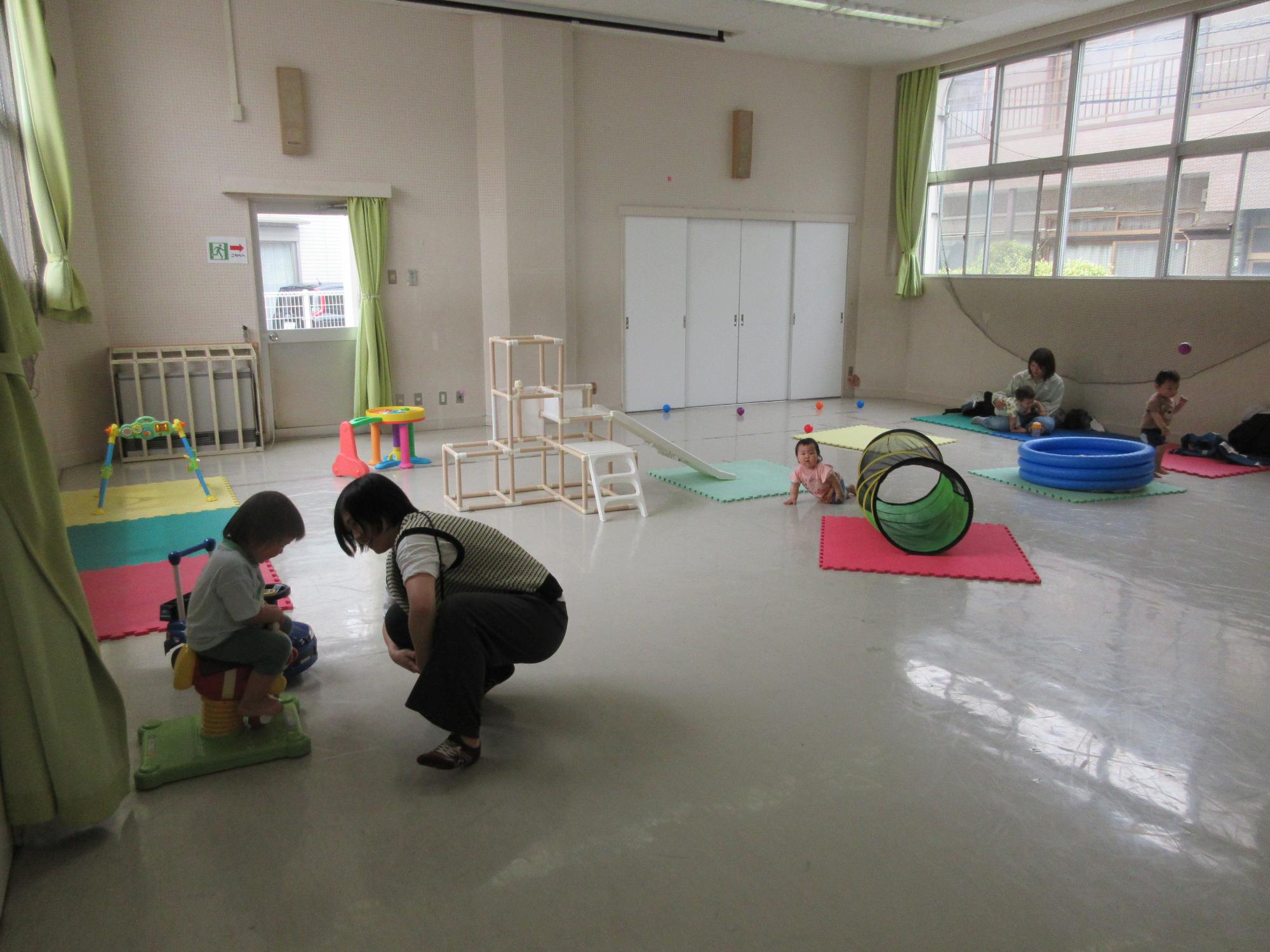幼児が遊具で遊び、お母さんが自分の子に話しかけている様子