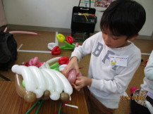 長机に置いた白色の風船でかごを一生懸命作っている男の子の写真