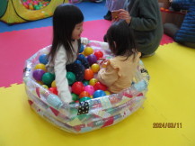 カラフルな色のボールが入った小さなビニール製のボールプールに2名の女の子が入り遊んでいる様子の写真