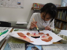子どもを挟んだ2名の大人の絵を描いた画用紙に、絵の具で色を塗っている女の子の写真