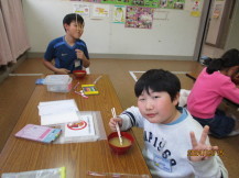 長机の端と手前に座った2名の男の子が、赤色のお椀に入った大根のお味噌汁を食べている写真