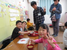 長机の左側に座った2名の子供と右側に座った女の子が、収穫したばかりの大根が入ったお味噌汁を美味しそうに食べている写真