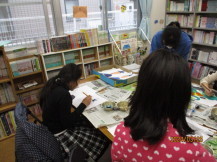 新聞紙を敷いたテーブルの席に座った女の子たちが、画用紙に書かれた紙しばいの絵に色を塗っている様子の写真
