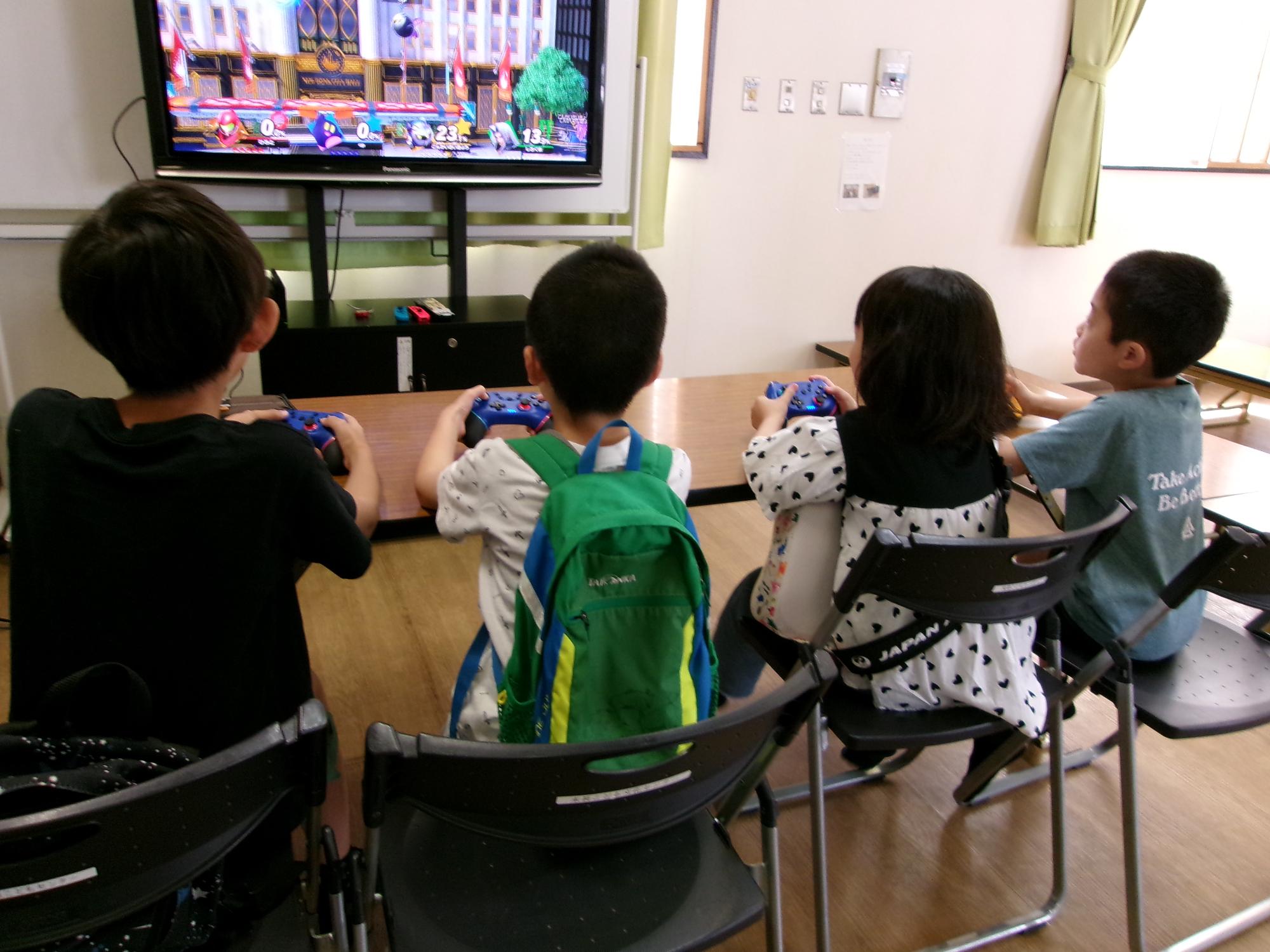 4人の子どもが並んでテレビモニターに映るゲームで遊んでいる写真