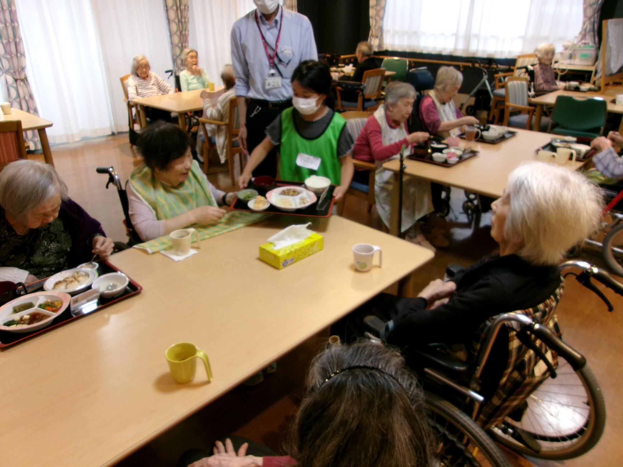 そんぽの家で利用者さんに昼食の配膳をお手伝いしている子どもの写真
