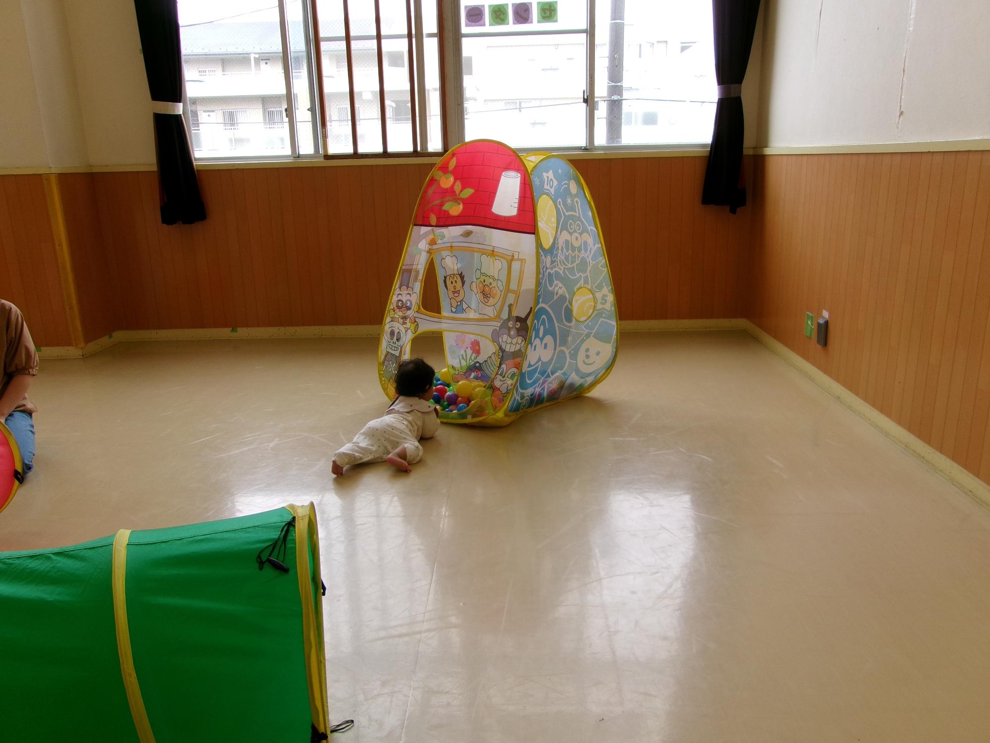 小さいボールがたくさん入っている小型テントに向かってハイハイしている幼児の写真