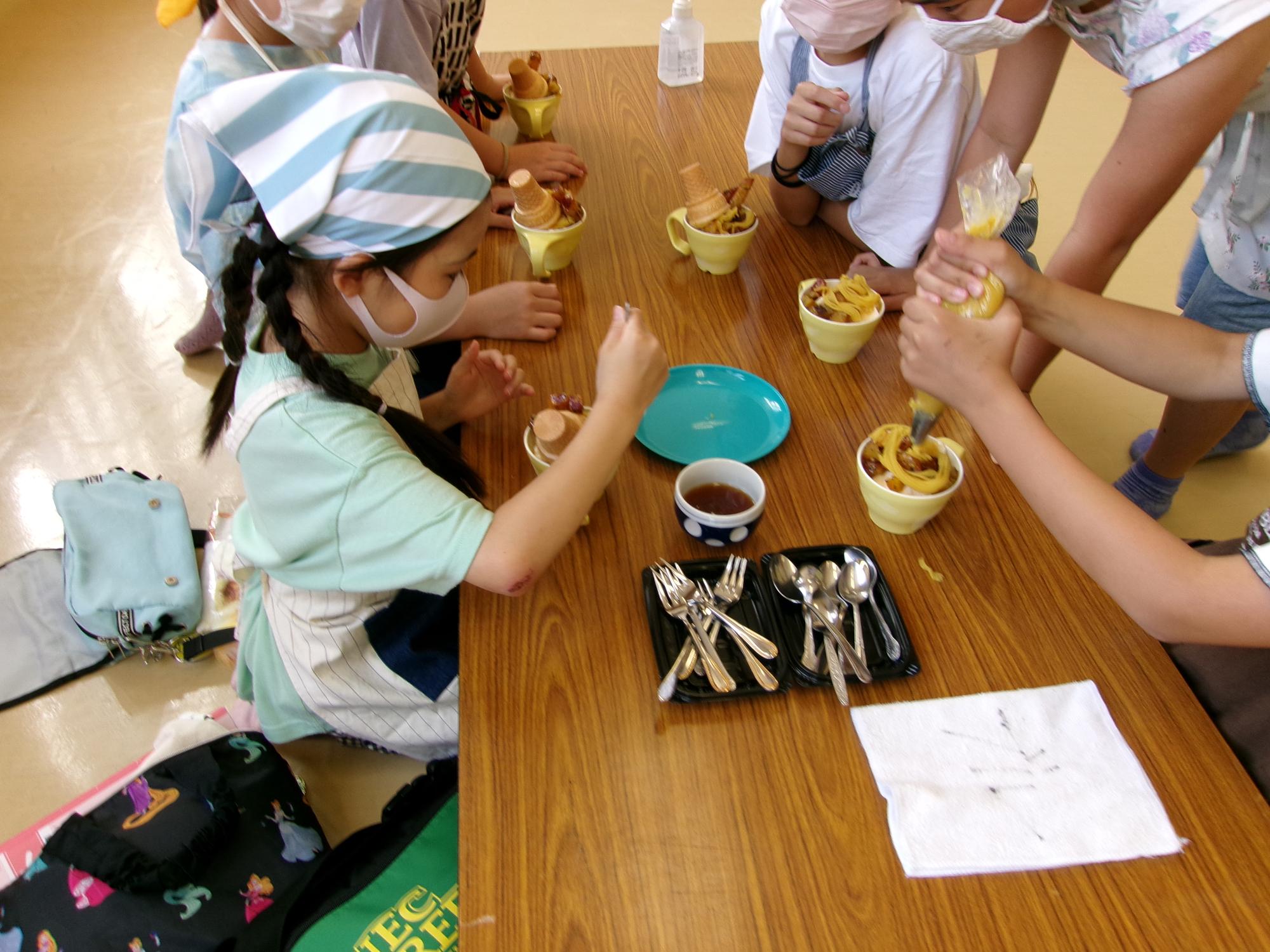 カップにアイスと大学芋を入れて混ぜ、上からさつまいもペーストを絞り器で絞っている写真