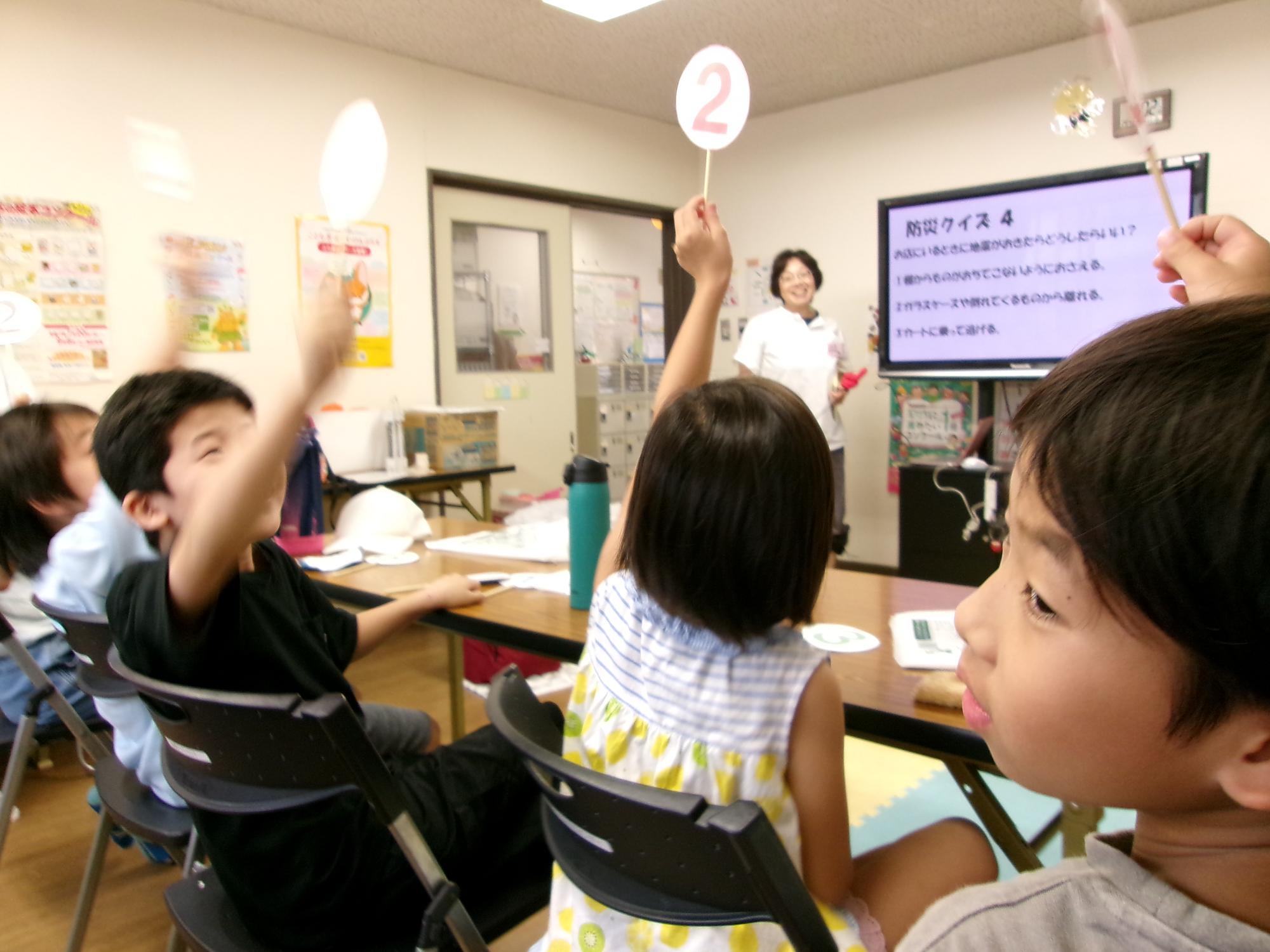 こどもたちが答えの札をあげクイズに答えている写真