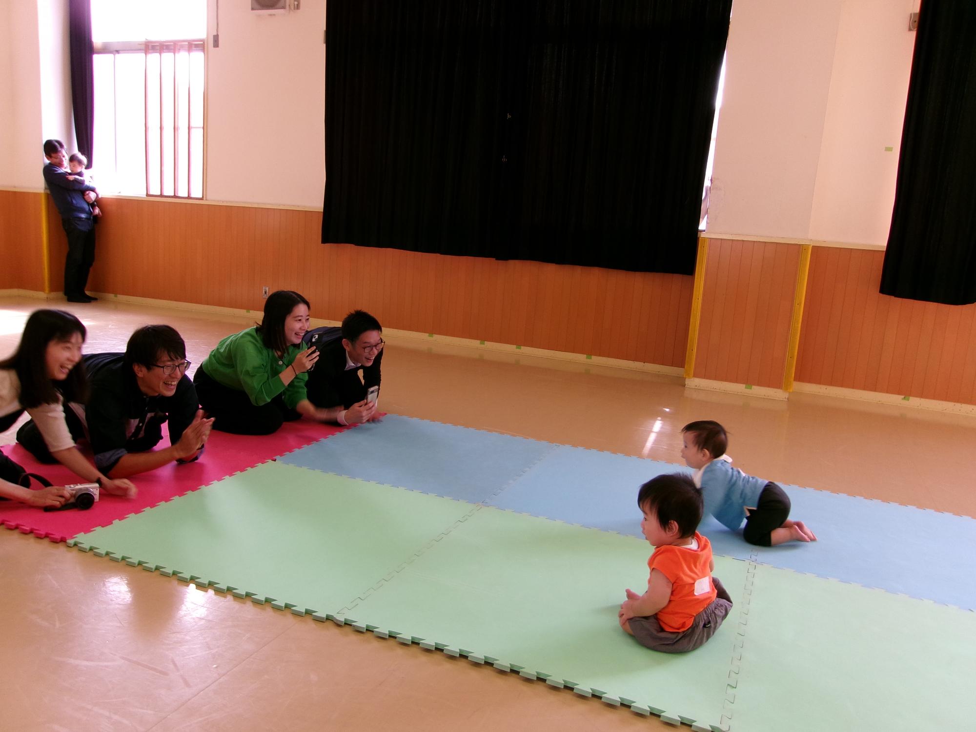 ハイハイする赤ちゃんと赤ちゃんを呼び込む父母の写真