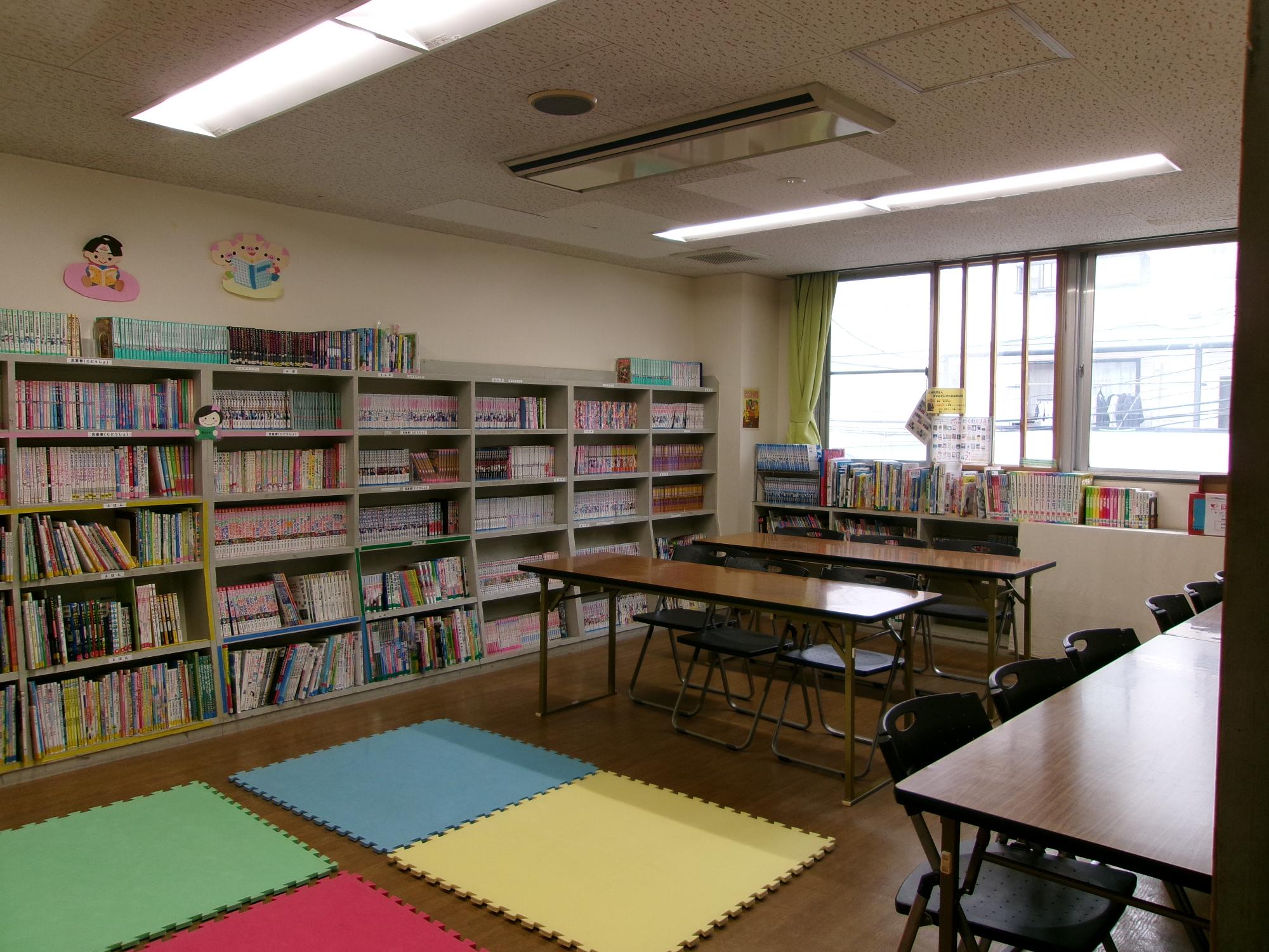 壁側に向かって2テーブル、中央に2テーブル、床面はマットが4面敷いてある図書室の写真
