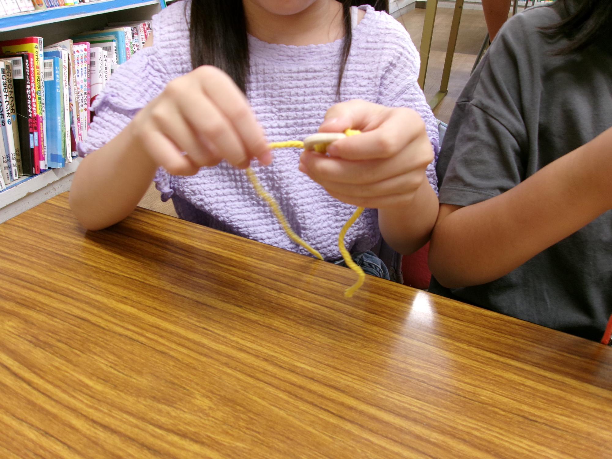 子どもが木の輪に紐を通して編んでいる写真