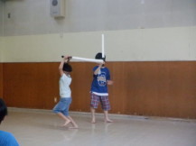 両手で持った棒を振り下ろす男の子と後ろで棒を片手で持ちながら見ている男の子の写真