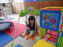 小さい遊具のブランコに乗り笑顔でカメラ目線の女の子を撮影した写真