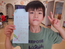 お父さんに向けたメッセージのサンクスカードを片手で持ちピースサインで撮影している男の子の写真
