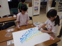青や黄色の紙を使い水しぶきを表現している女の子と作業を横で見ている女の子の写真