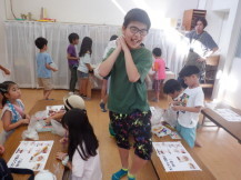 周りの子供たちが座って作業する中緑の服の男の子が肩に担いだ材料を一生懸命運んでいる写真
