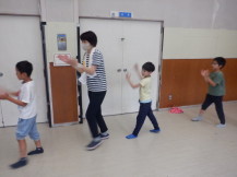 楽しそうに踊る3人の子供たちと首にタオルをかけながら踊る女性の写真
