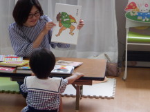 1人の子供に笑顔で絵本の表紙を見せているもっちゃん先生の写真
