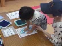 手形スタンプの紙に両手でしっかりと押し当てる女の子と横で見守る母親の写真