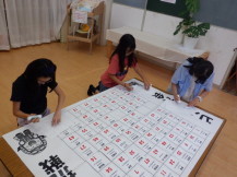 大きなビンゴ表を3人で手分けして作業する女の子を斜め上から撮っている写真