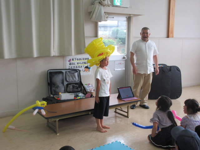 バルーンで作られた大きな帽子をかぶった男の子と講師の写真