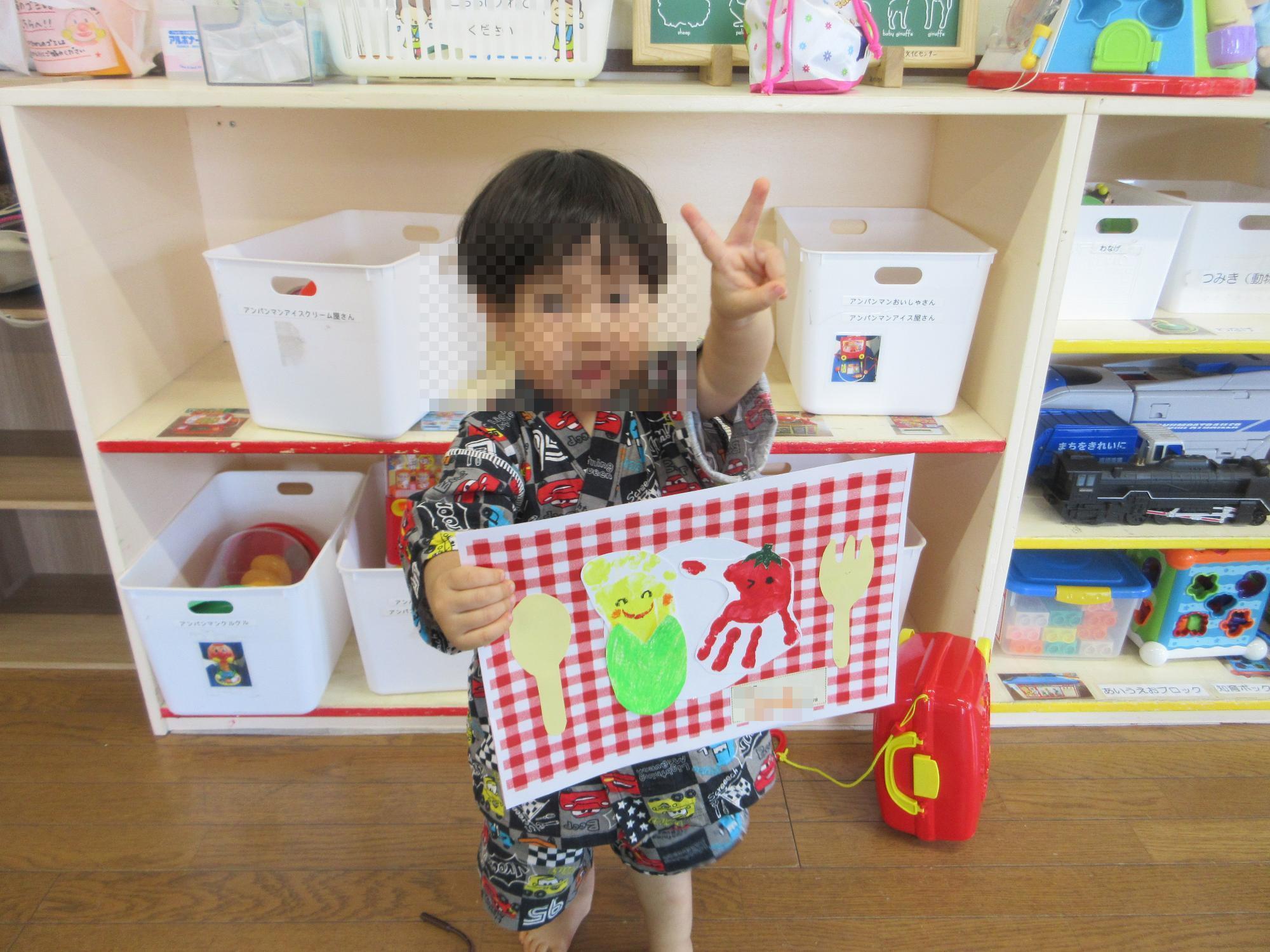野菜に見立てた手形・足形の紙をもってピースする乳幼児