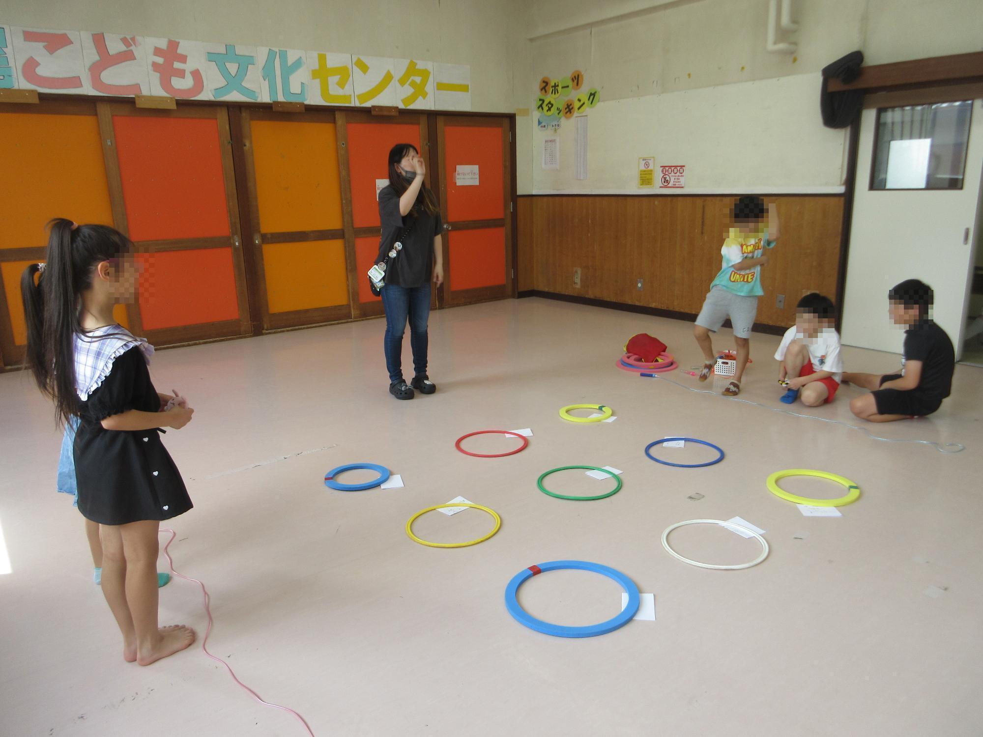 フープの列と、子どもたちが次のゲームの説明を聞いているようす