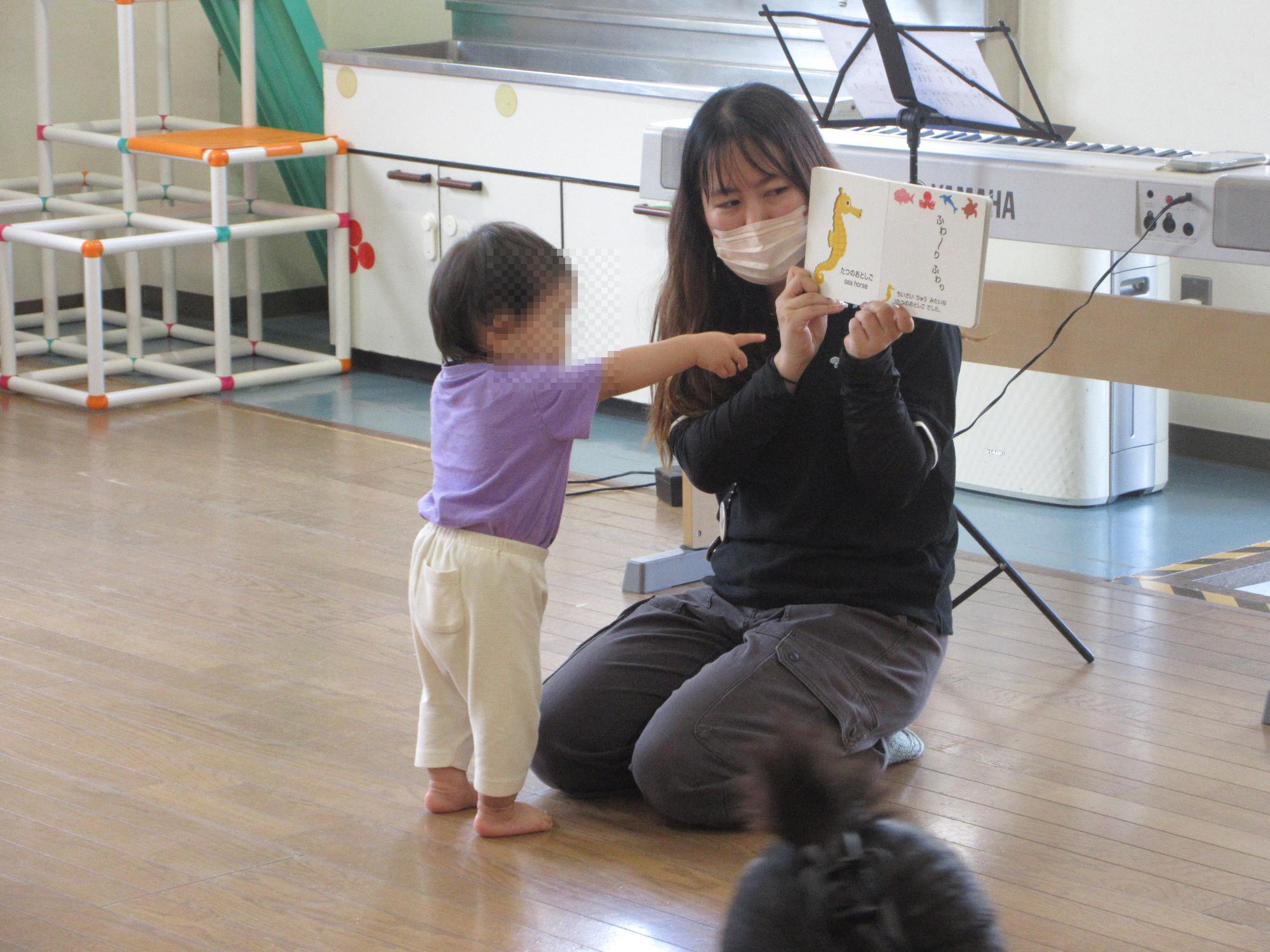 スタッフが音読している本を指さす乳幼児