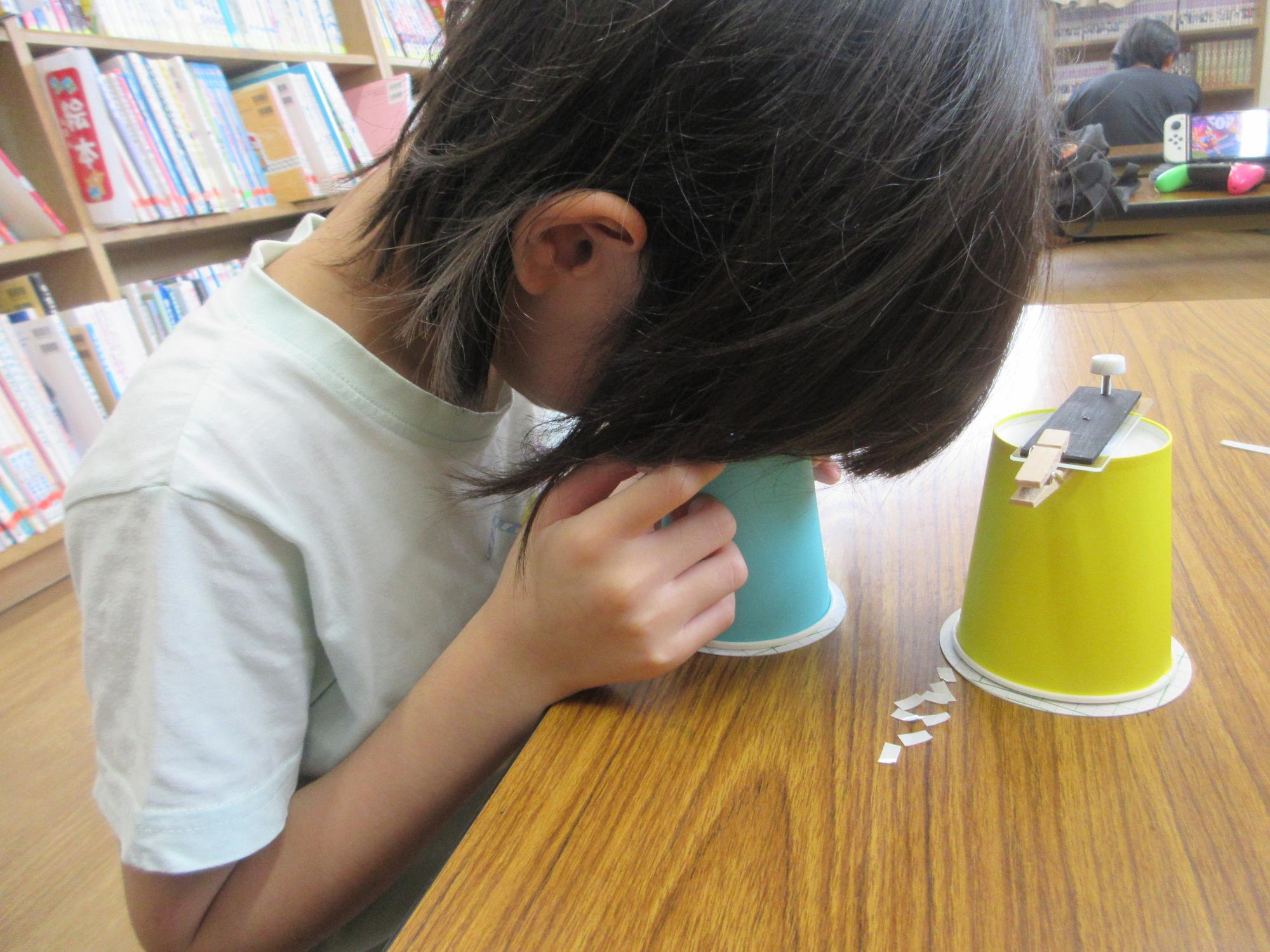 紙コップで作った顕微鏡をのぞき込む児童のようす