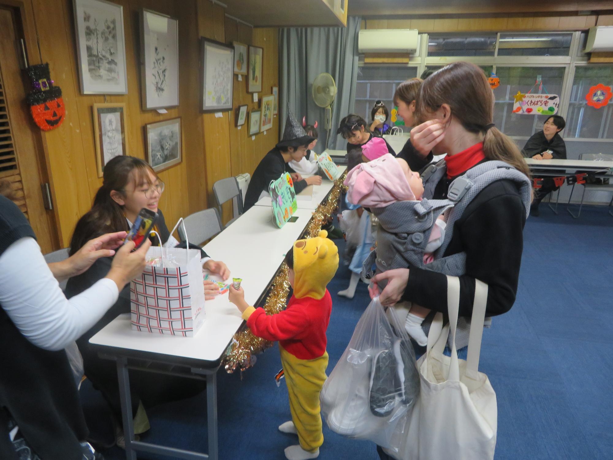 ディズニーキャラクターの仮装をしたこどもたちが映画キャラクターの仮装をしたボランティアからお菓子をもらっている写真