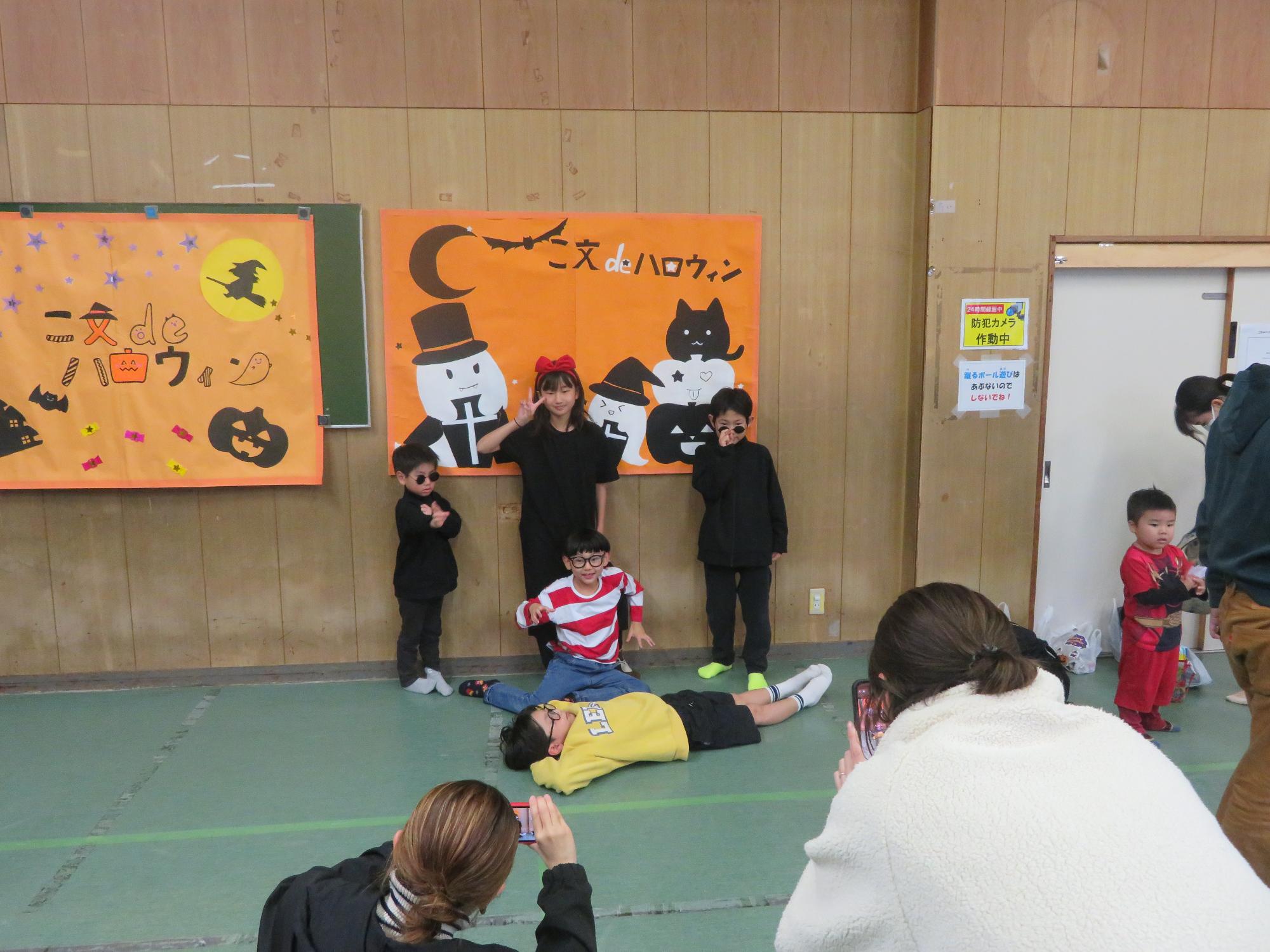 アニメキャラクターの仮装をしたこどもが壁面飾りの前でなりきりポーズをとりながら写真を撮っている写真