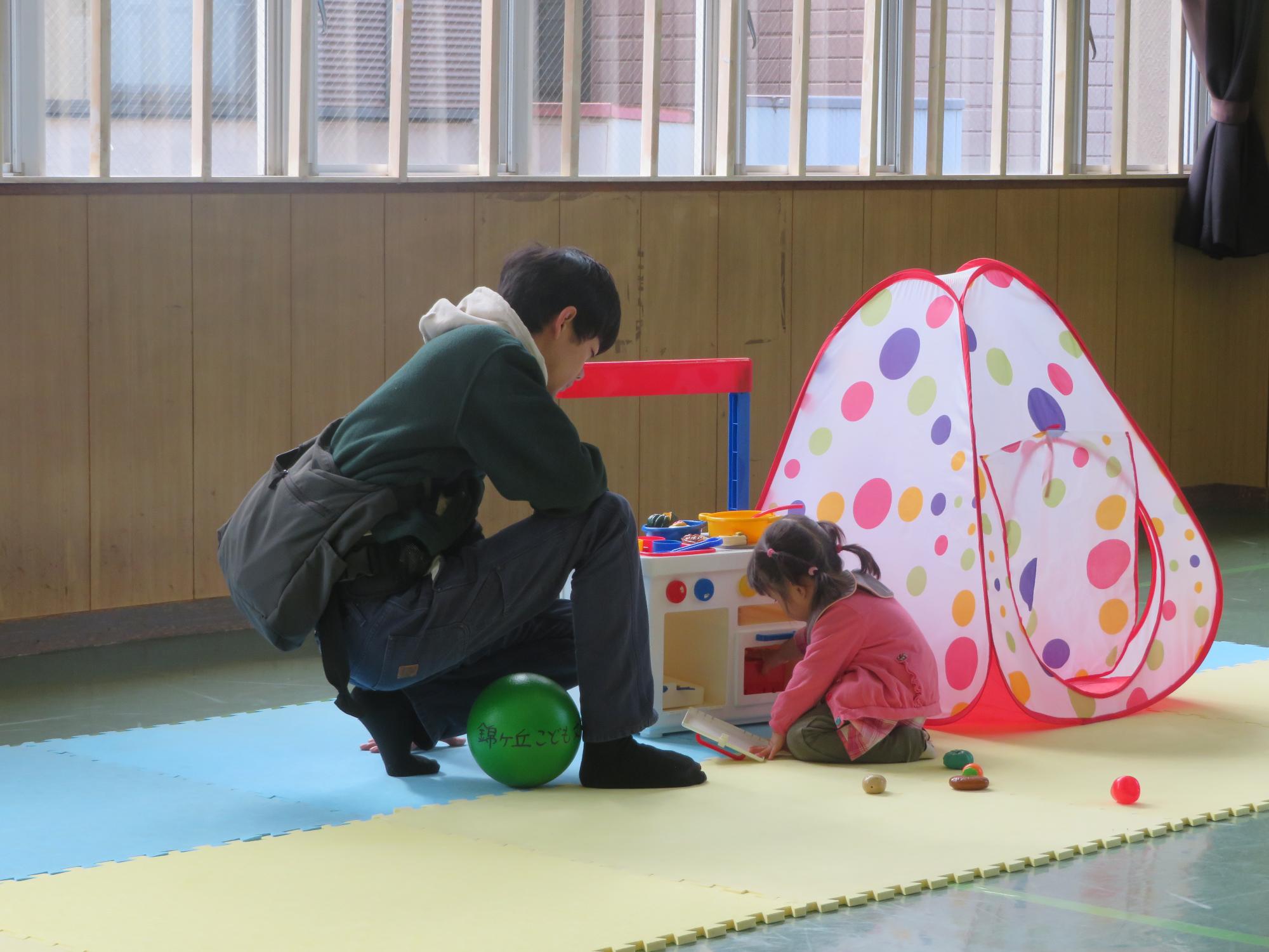 おままごとセットで遊ぶ幼児と保護者の写真