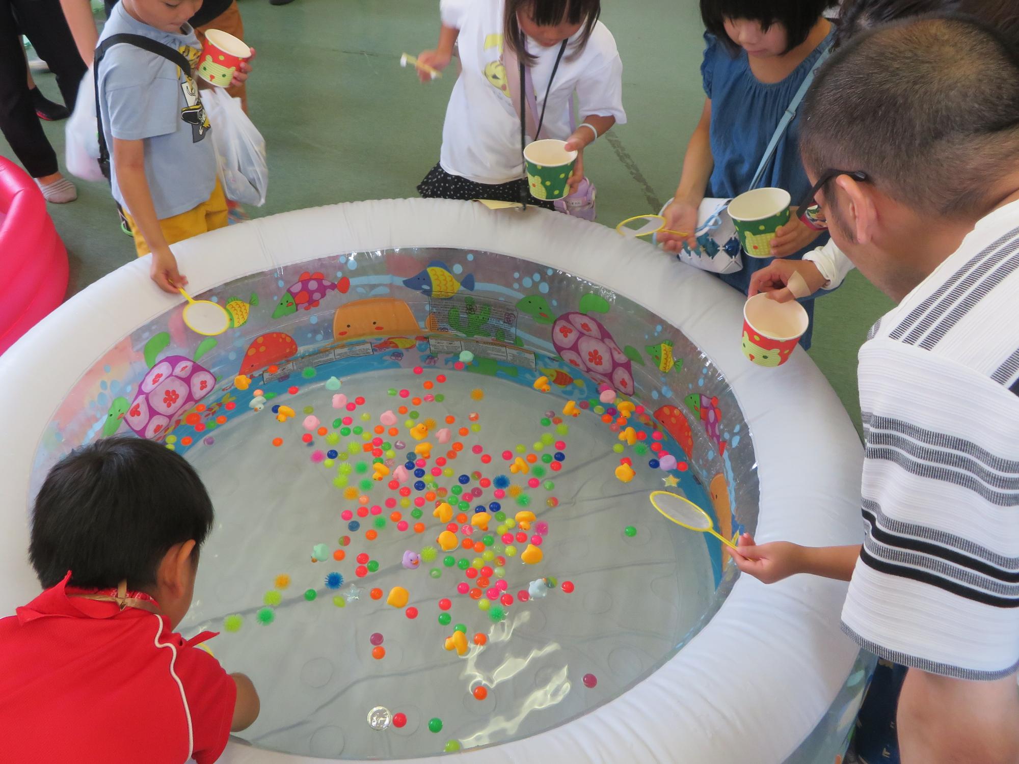うきうきすくいコーナーでプールを囲んでスーパーボールすくいをする子どもたちの写真
