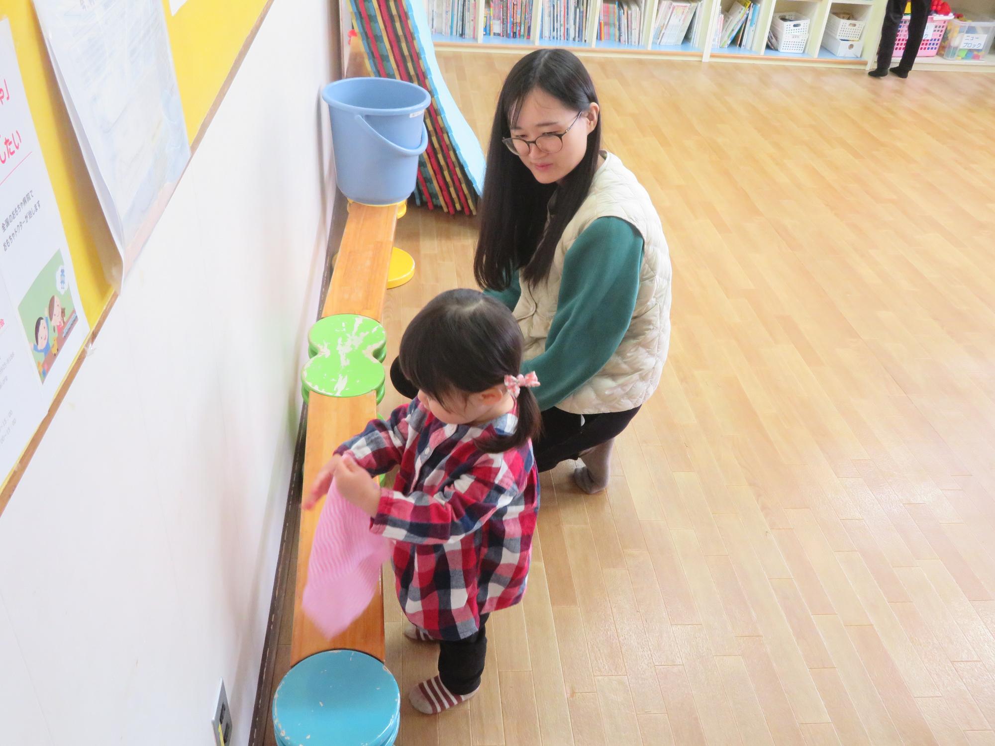 乳幼児室で平均台を拭く幼児と保護者の写真