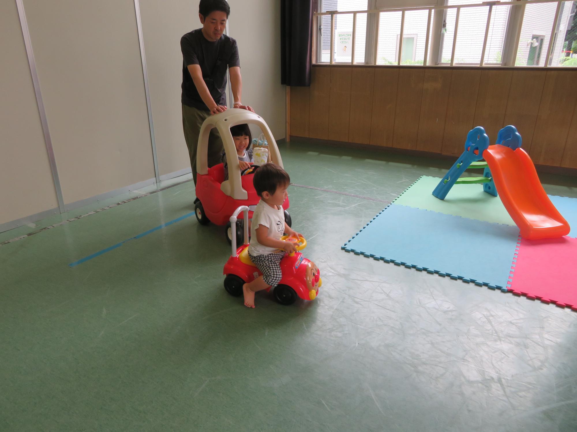 車の乗り物で遊ぶ幼児たちと保護者の写真