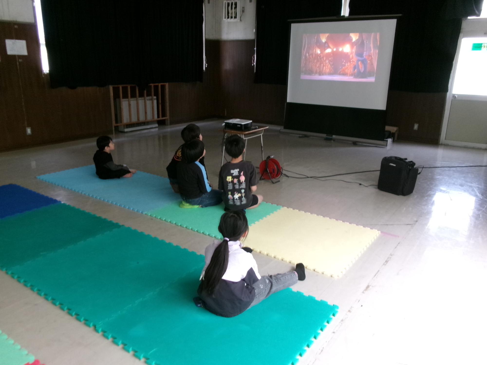 児童が大きなスクリーンで上映している映画を観ている様子の写真
