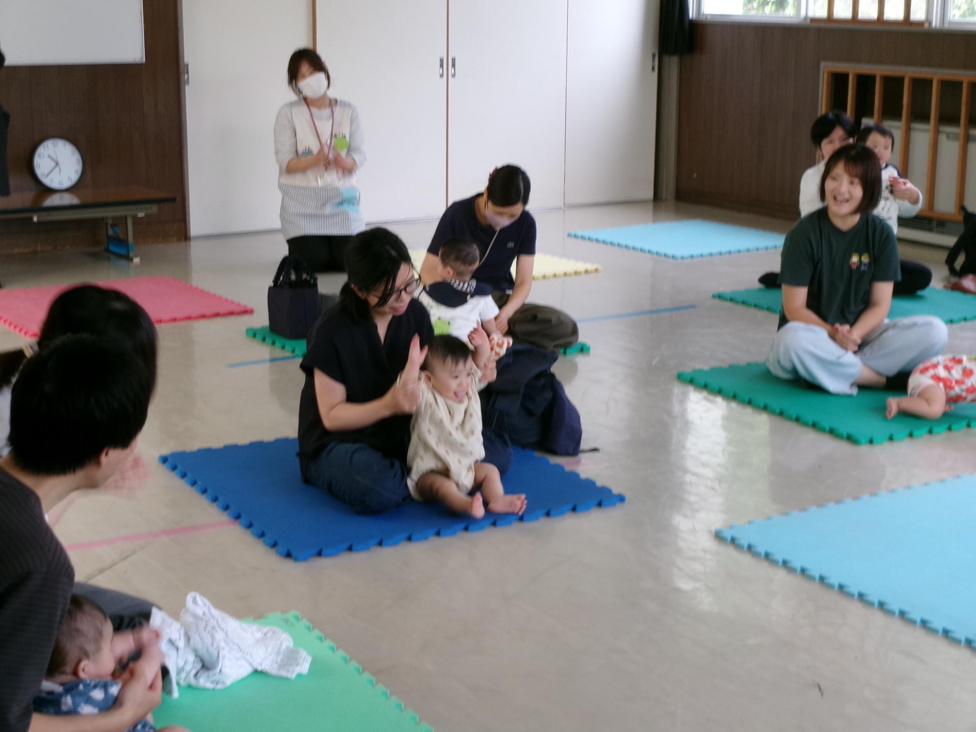 自己紹介をしている乳幼児親子をまわりの親子がほほえましく見ている様子の写真