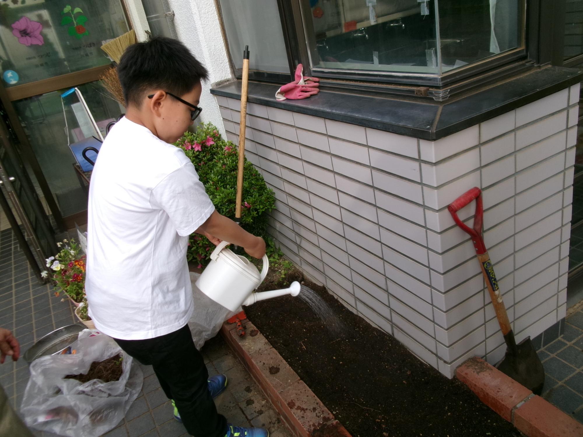 小学生が種を植えたあとの花壇に水を撒いている様子の写真