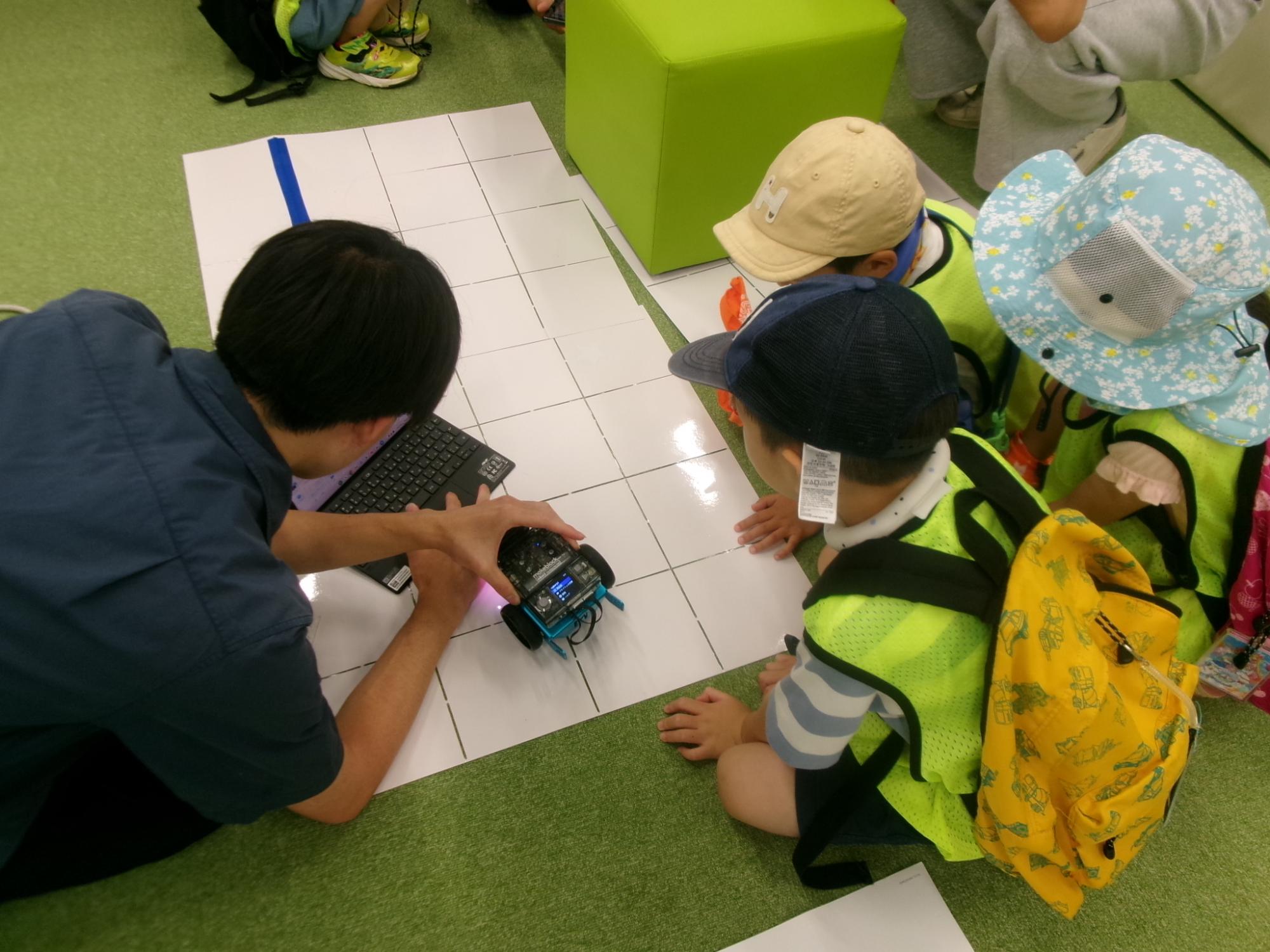 児童が大学生から走行するロボットのプログラミングのレクチャーを受けている様子