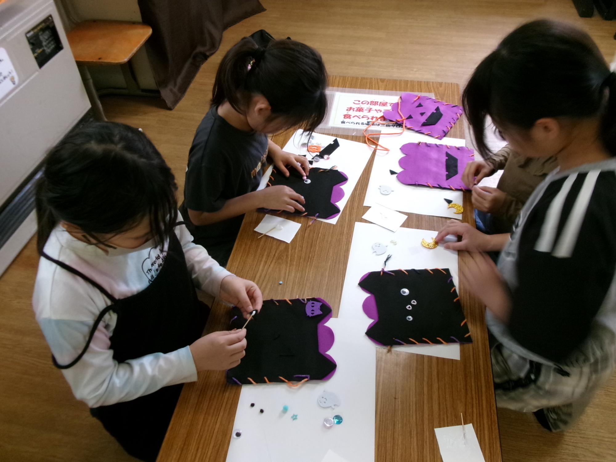 子どもが猫の形に切ったフェルトでバッグを作っている様子の写真