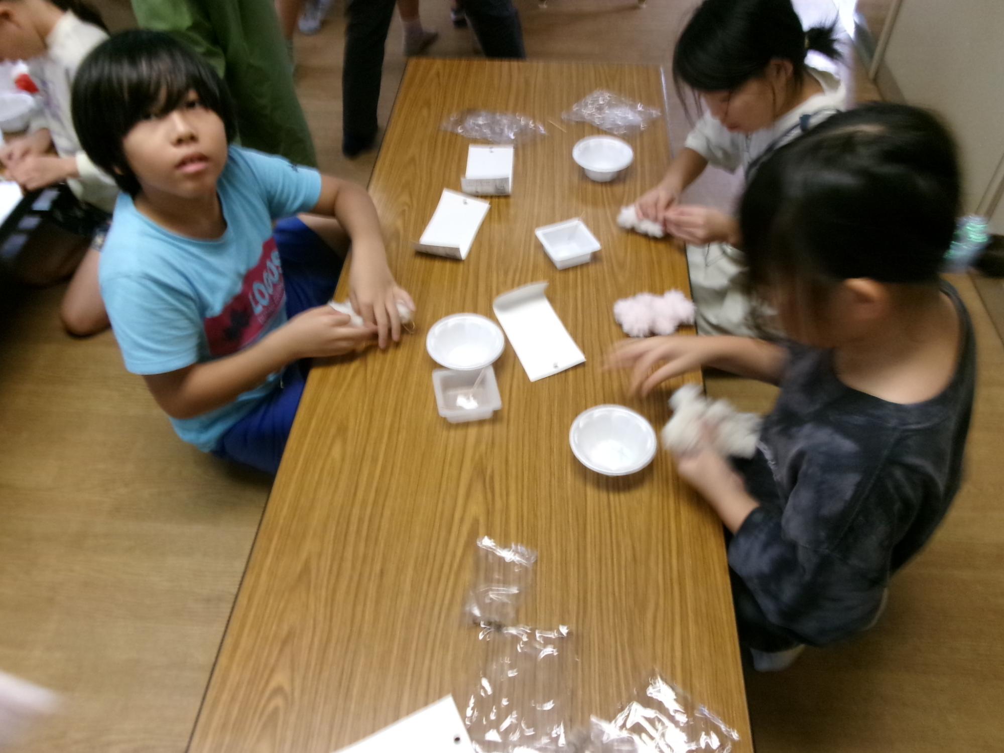 児童がモールを編み込んで人形を作っている様子の写真