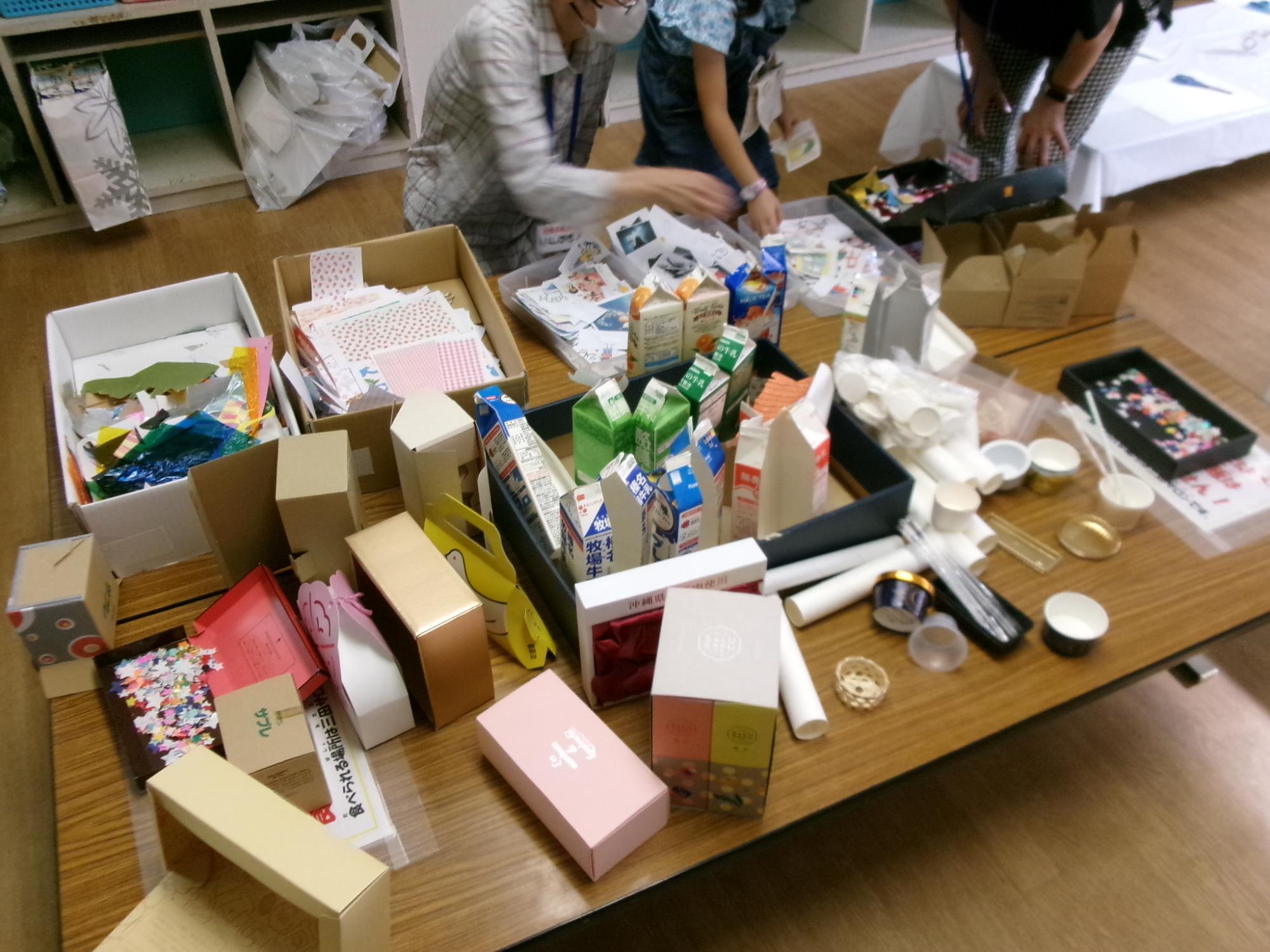 机いっぱいに置かれた牛乳パックやカップなどの工作材料の写真