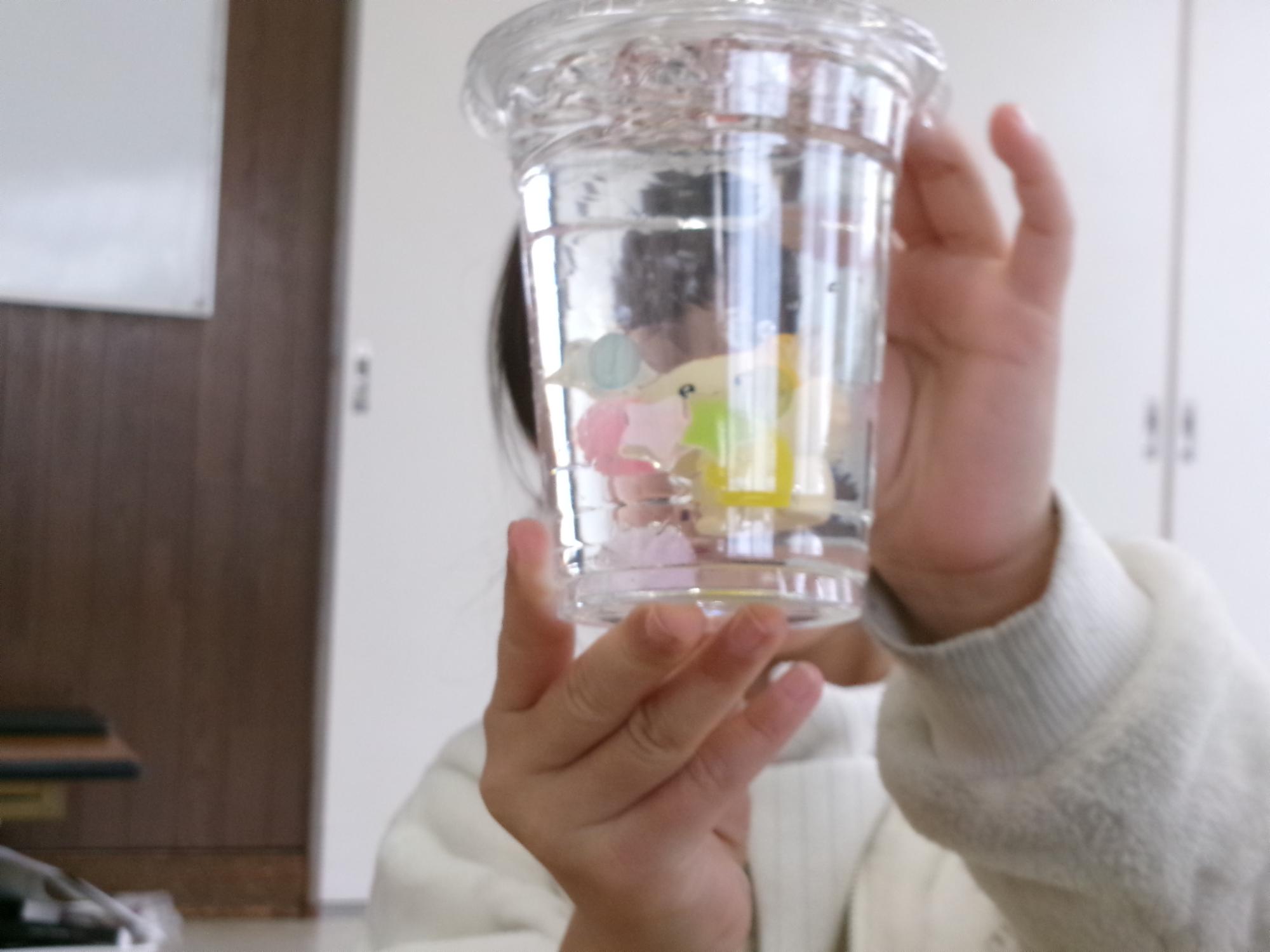 プラスチックのコップの中に水と消臭ビーズとオーナメントをいれたボトルを持っている小学生の様子の写真
