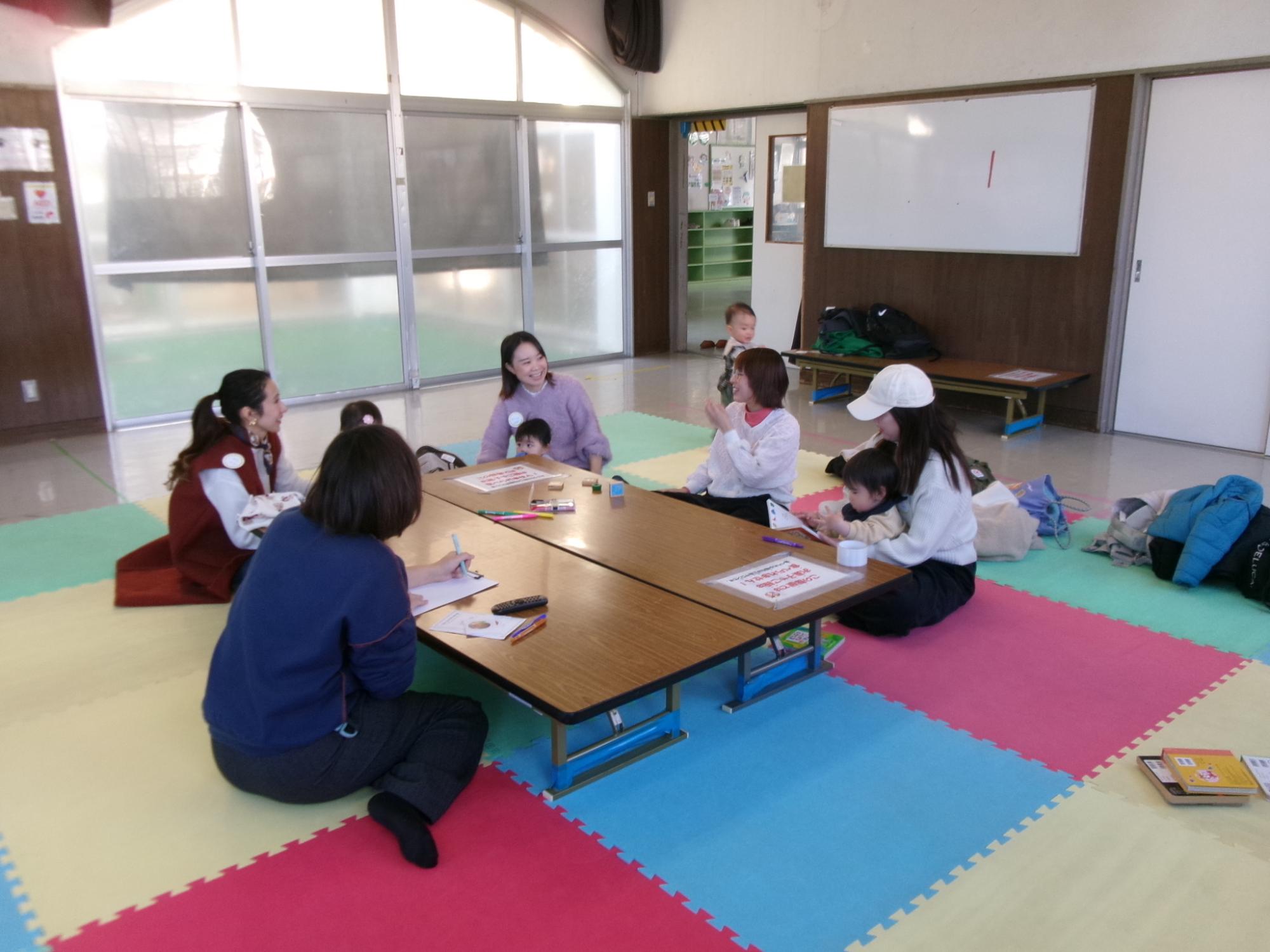 マットの上で談笑をしている幼児親子の写真