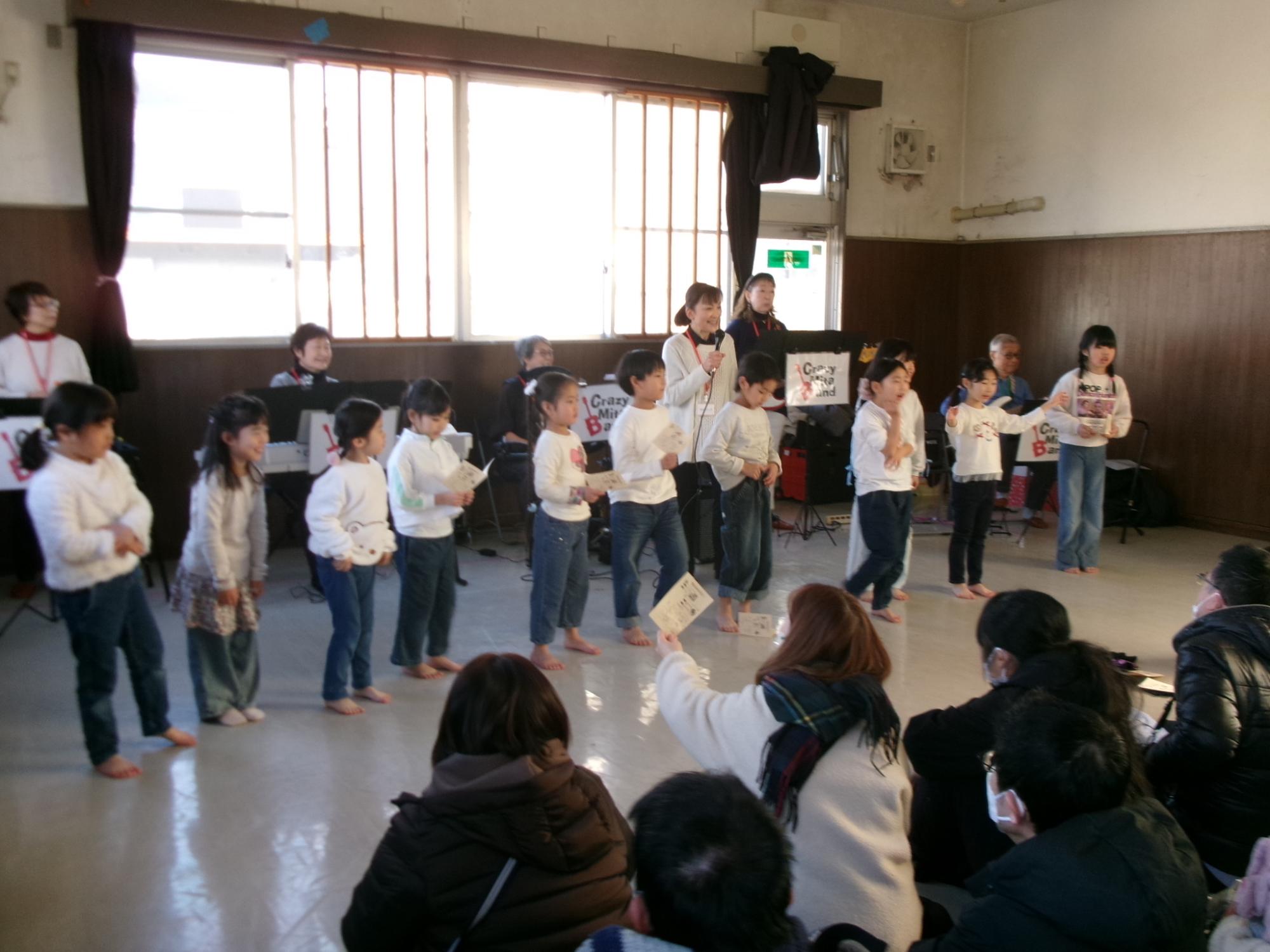 クレイジーミタバンドの皆さんと、演奏に合わせて一緒に歌を歌っている子どもたちの写真